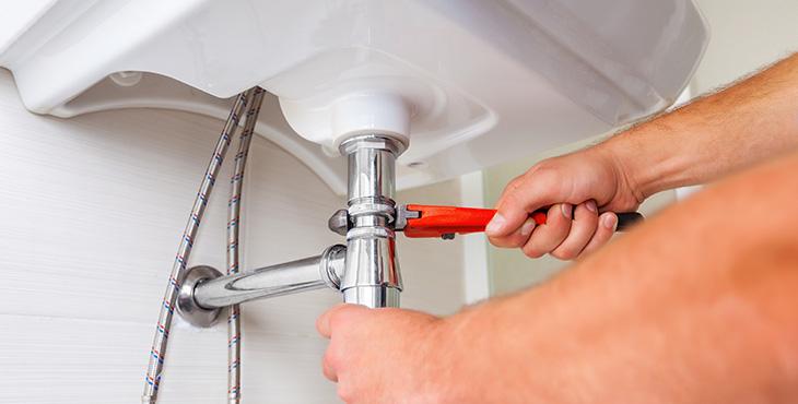 man fixes bathroom sink pipe with a wrench